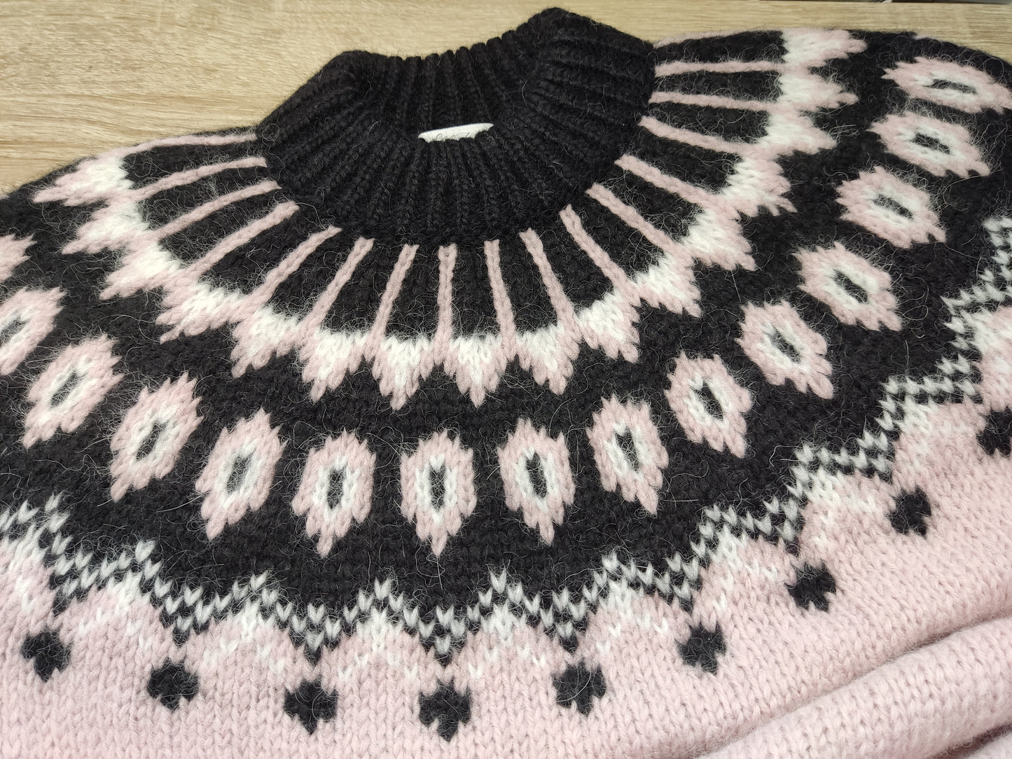 Hand-knitted pale rose pink women’s Scandinavian Lopapeysa sweater with a fluffy black and white Nordic round yoke, featuring black ribbed cuffs, collar, and hem, made from soft hypoallergenic baby alpaca, merino wool, and kid mohair.