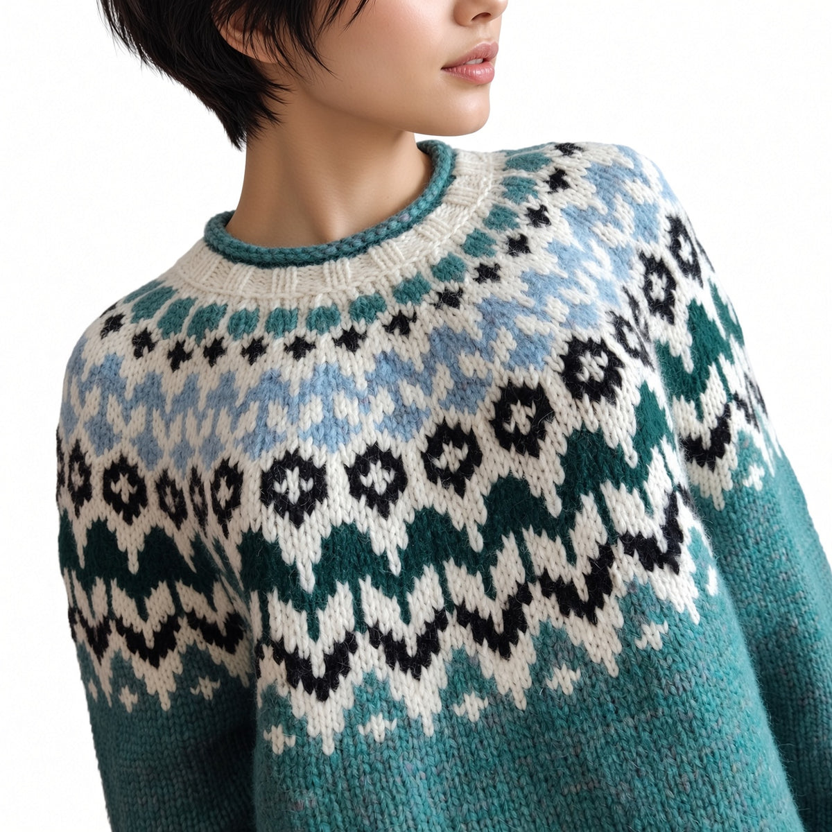 A close-up of a person wearing a knitted crewneck sweater with a Fair Isle pattern in teal, cream, light blue, and black, against a plain white background.