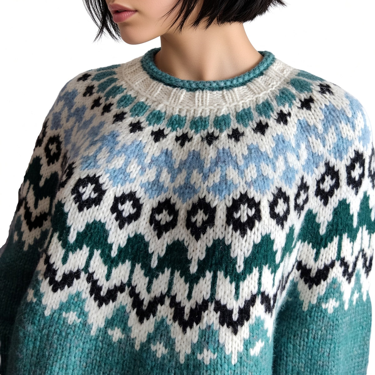 A close-up of a person wearing a chunky knit crewneck sweater with a Fair Isle pattern in teal, light blue, black, and off-white.