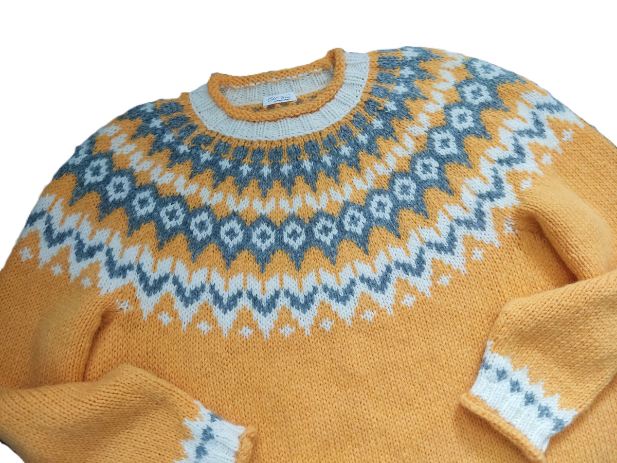 A close-up of a knit crewneck sweater in mustard yellow with a blue and white Fair Isle pattern across the chest and shoulders.