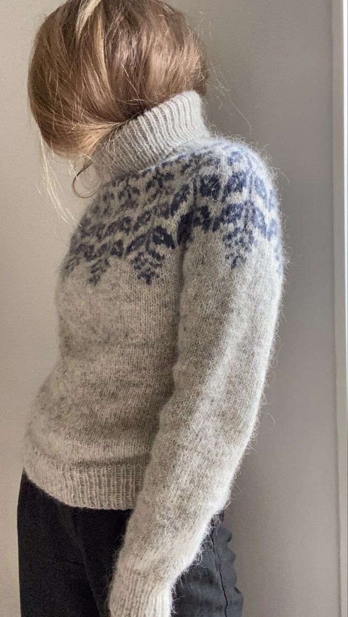 Person wearing a knitted sweater with a pattern against a plain background
