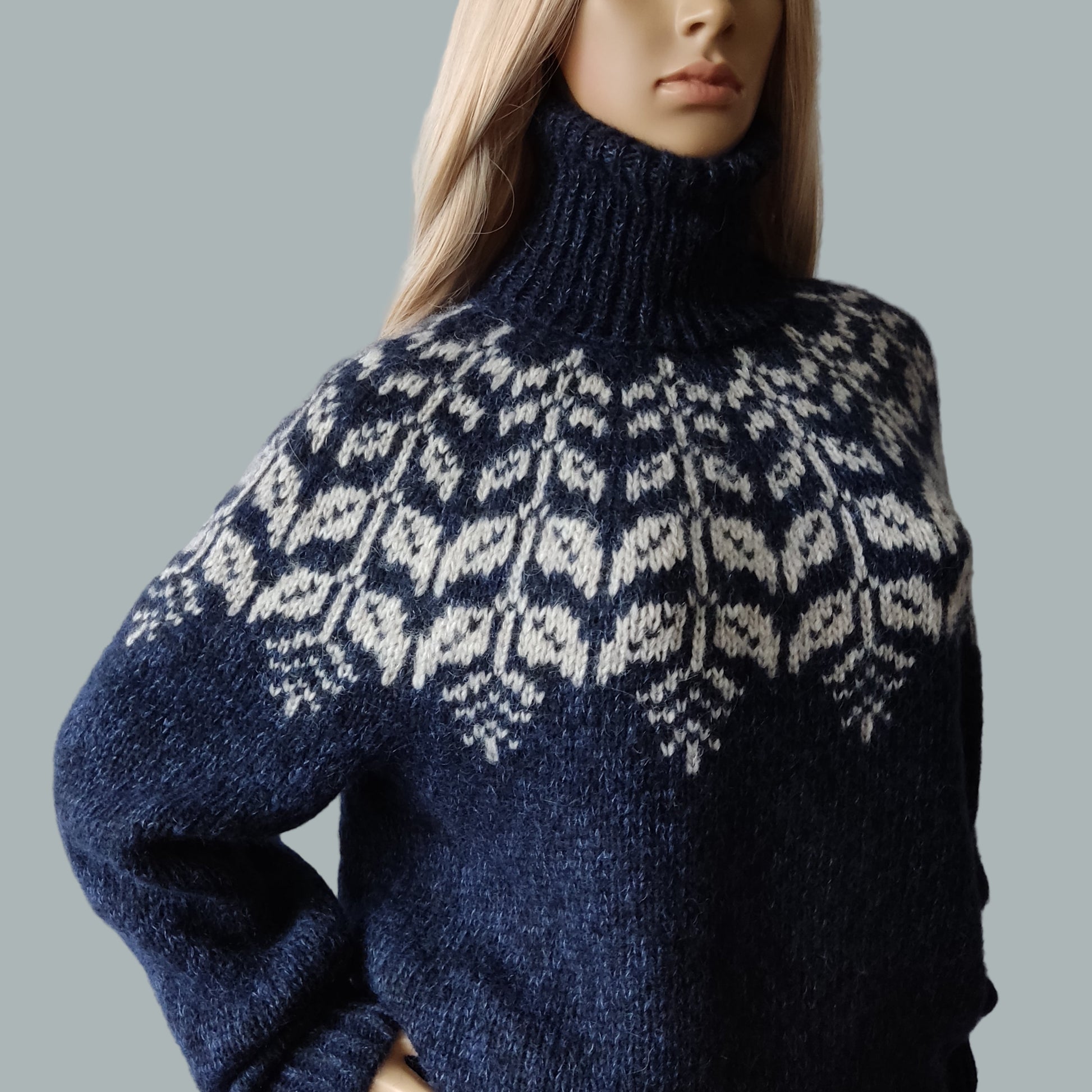 Mannequin wearing a blue knitted sweater with a pattern against a gray background