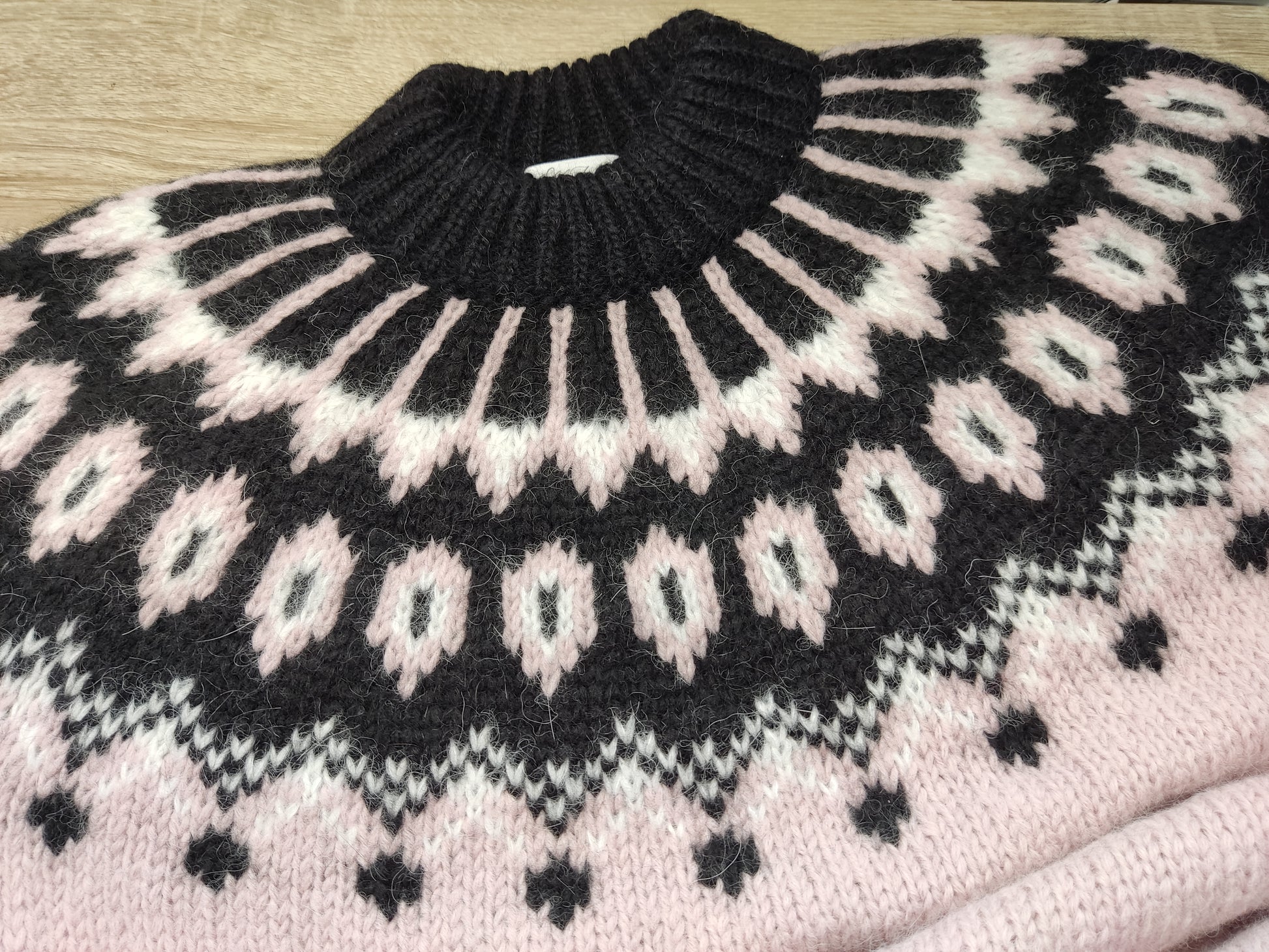 Hand-knitted pale rose pink women’s Scandinavian Lopapeysa sweater with a fluffy black and white Nordic round yoke, featuring black ribbed cuffs, collar, and hem, made from soft hypoallergenic baby alpaca, merino wool, and kid mohair.