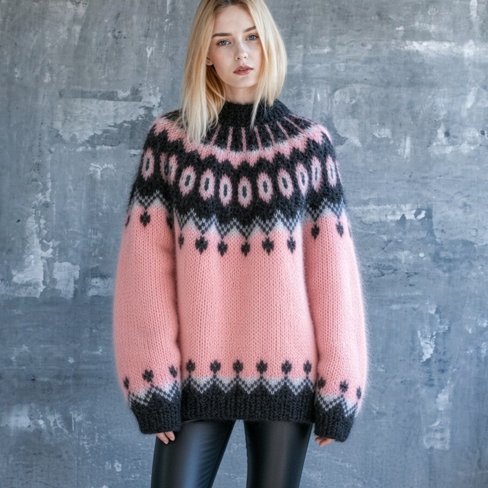 A woman wearing a pink and black knit sweater with a Fair Isle pattern, standing against a textured gray concrete wall.