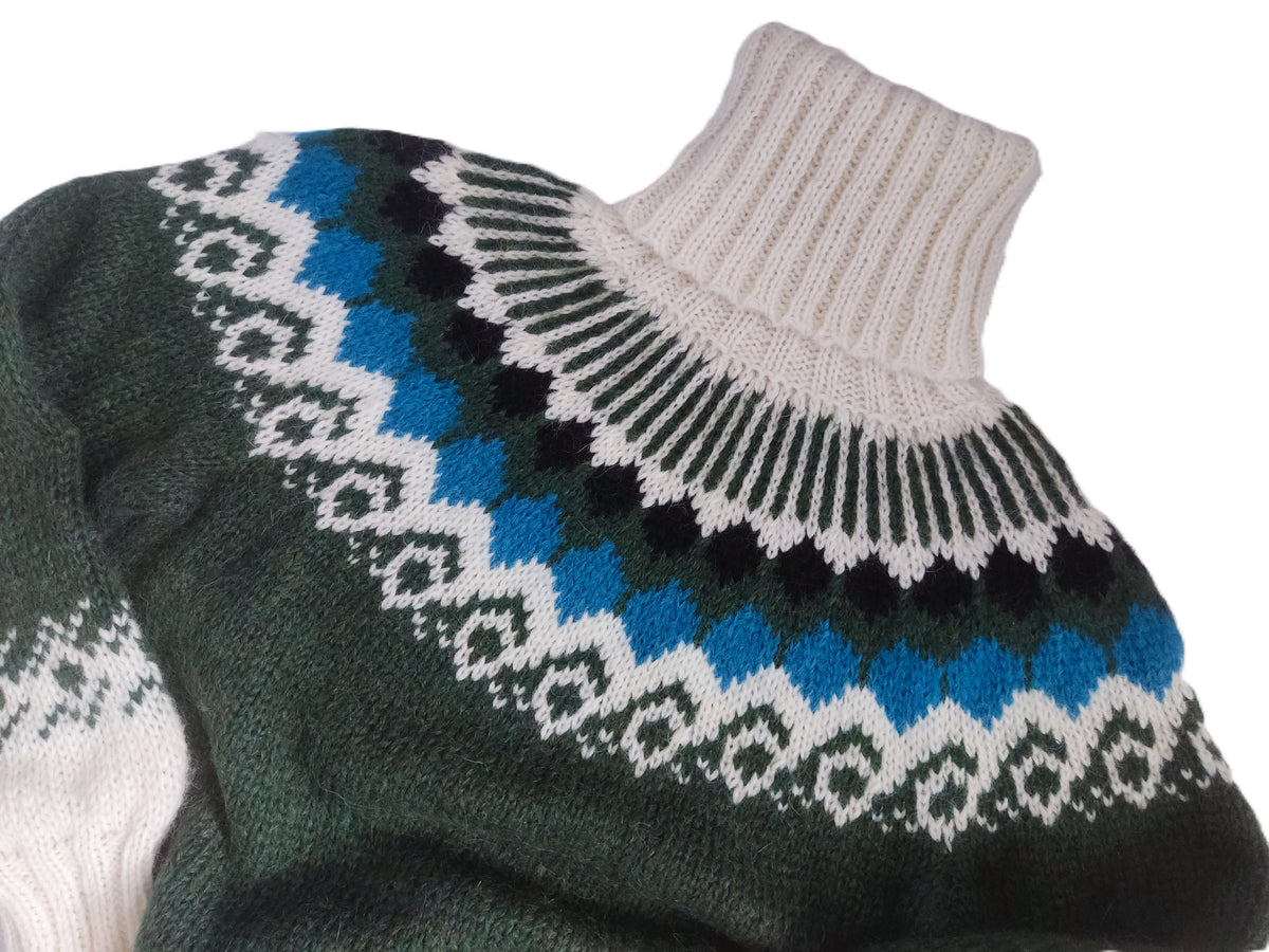 A close-up of a knit sweater on a white mannequin torso, featuring a dark green base with a Fair Isle yoke pattern in cream, black, and bright blue, finished with a cream ribbed turtleneck.