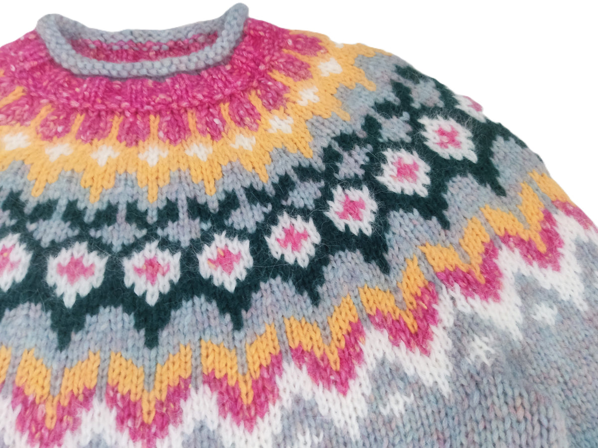 A close-up of a hand-knit sweater featuring a colorful Fair Isle pattern with pink, yellow, dark green, white, and light blue yarns.