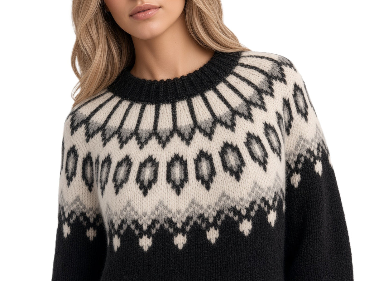 A close-up  of a woman modeling a black knit sweater with a cream Fair Isle pattern across the chest and shoulders against a white background.