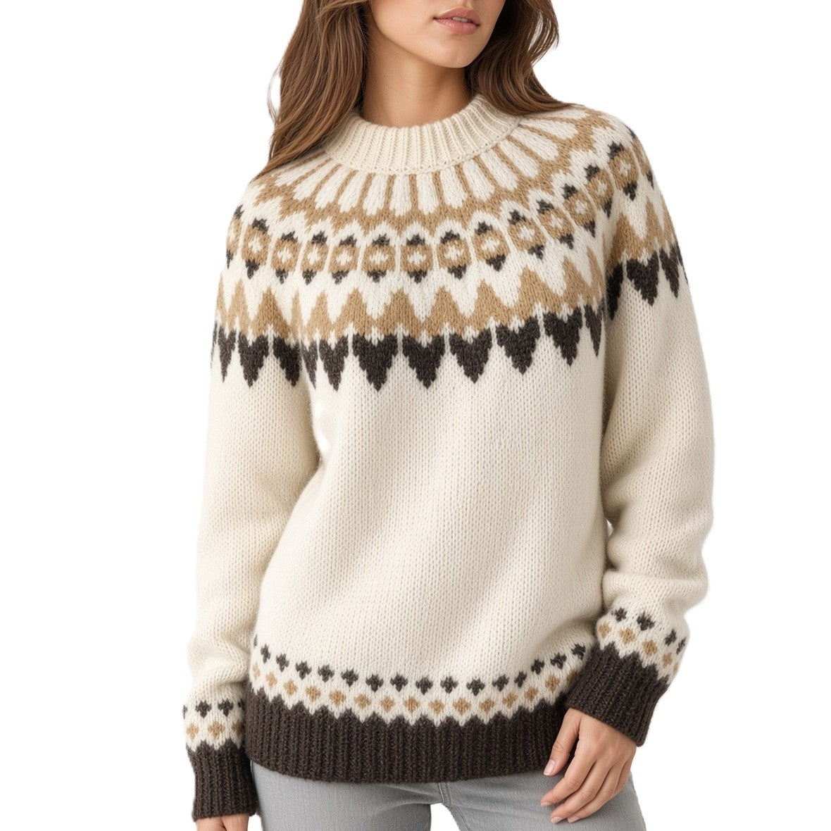 A woman wearing a cream-colored knit sweater with a brown and tan Fair Isle pattern across the chest and cuffs, paired with light gray jeans against a white studio background.
