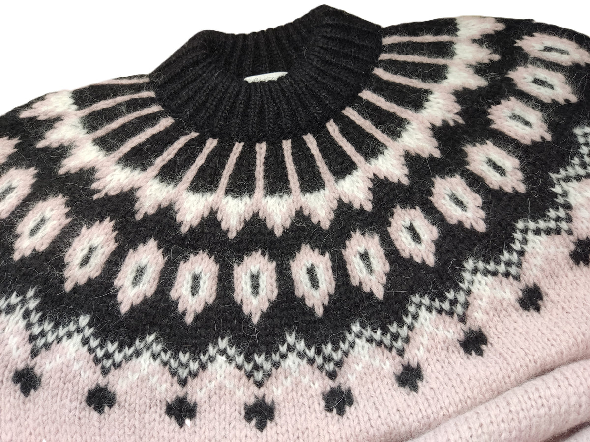 A close-up of a knit sweater featuring a black ribbed crew neck and a Fair Isle style pattern in black, cream, and light pink.