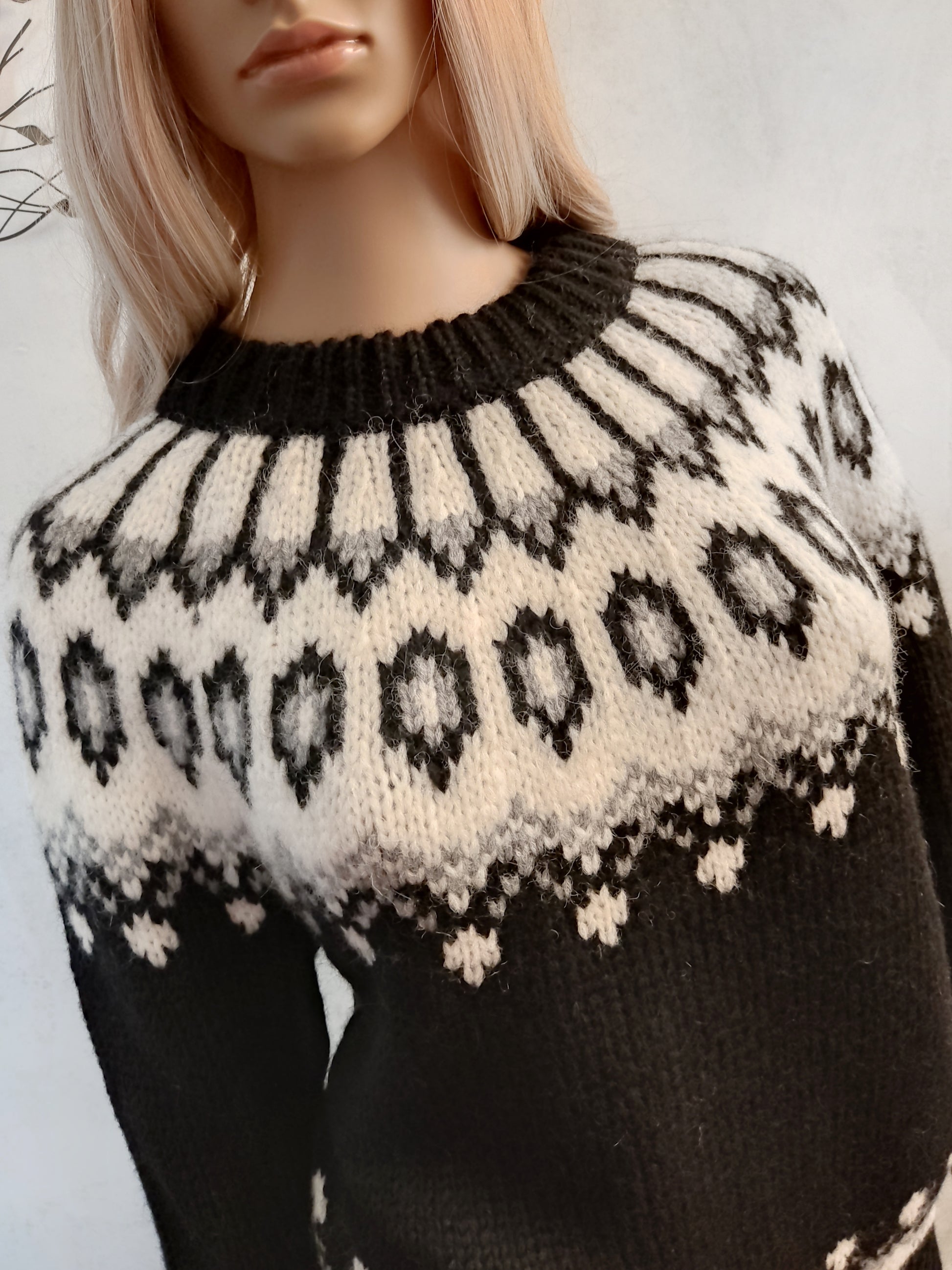 Hand-knitted black oversized unisex Scandinavian Lopapeysa sweater with a thick-knit white and gray Nordic round yoke, featuring black ribbed cuffs, collar, and hem, made from soft hypoallergenic baby alpaca and merino wool.